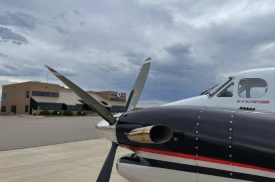 Plane on tarmac with propeller, overcast sky, and building in background.